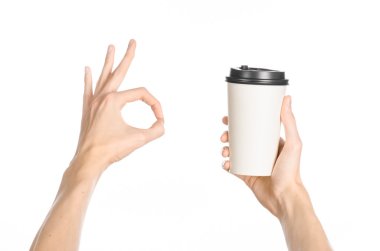 Breakfast and coffee theme: man's hand holding white empty paper coffee cup with a brown plastic cap isolated on a white background in the studio, advertising of coffee first-person view