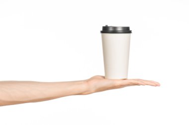 Kahvaltı ve kahve teması: Stüdyoda beyaz bir arka planda izole edilmiş kahverengi plastik şapkalı beyaz, boş bir kahve fincanı tutan bir adamın eli, kahve reklamı yapıyor.