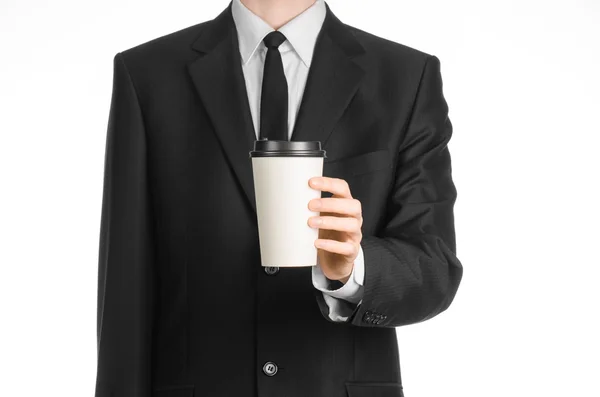 Almuerzos de negocios tema de café: hombre de negocios en un traje negro sosteniendo una taza de papel blanco de café con una tapa de plástico marrón aislado sobre un fondo blanco en el estudio, publicidad de café — Foto de Stock