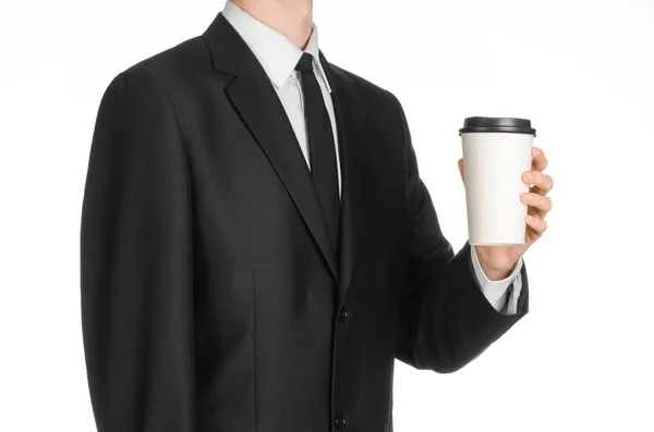 Business lunches coffee theme: businessman in a black suit holding a white blank paper cup of coffee with a brown plastic cap isolated on a white background in the studio, advertising coffee — Stockfoto
