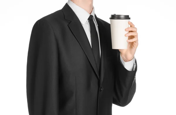 Business lunches coffee theme: businessman in a black suit holding a white blank paper cup of coffee with a brown plastic cap isolated on a white background in the studio, advertising coffee — Stok fotoğraf
