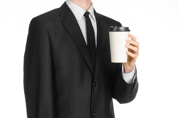 Business lunches coffee theme: businessman in a black suit holding a white blank paper cup of coffee with a brown plastic cap isolated on a white background in the studio, advertising coffee — Zdjęcie stockowe