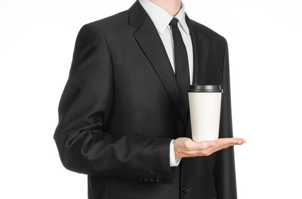 Almuerzos de negocios tema de café: hombre de negocios en un traje negro sosteniendo una taza de papel blanco de café con una tapa de plástico marrón aislado sobre un fondo blanco en el estudio, publicidad de café — Foto de Stock