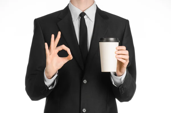 Business lunches coffee theme: businessman in a black suit holding a white blank paper cup of coffee with a brown plastic cap isolated on a white background in the studio, advertising coffee — 스톡 사진