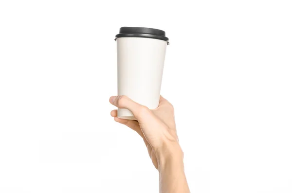 Breakfast and coffee theme: man's hand holding white empty paper coffee cup with a brown plastic cap isolated on a white background in the studio, advertising of coffee first-person view