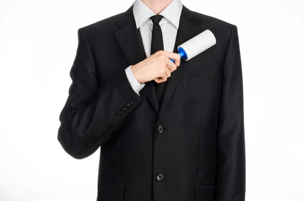 Dry cleaning and business theme: a man in a black suit holding a blue sticky brush for cleaning clothes and furniture from dust isolated on white background in studio. — Stockfoto