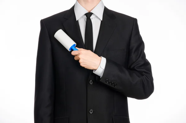 Dry cleaning and business theme: a man in a black suit holding a blue sticky brush for cleaning clothes and furniture from dust isolated on white background in studio. — Stockfoto