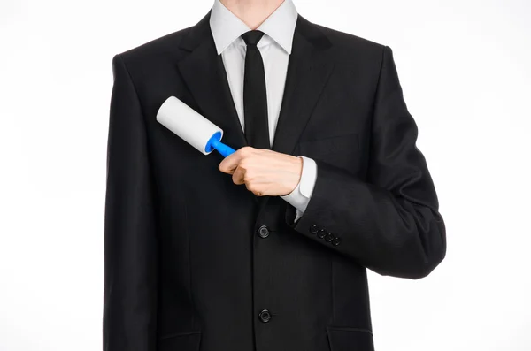Dry cleaning and business theme: a man in a black suit holding a blue sticky brush for cleaning clothes and furniture from dust isolated on white background in studio. — Stockfoto