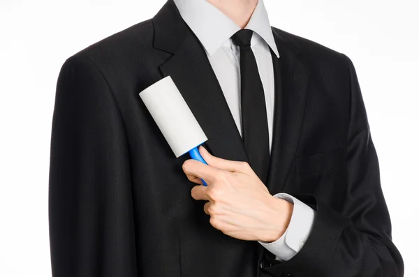 Dry cleaning and business theme: a man in a black suit holding a blue sticky brush for cleaning clothes and furniture from dust isolated on white background in studio. — Stok fotoğraf