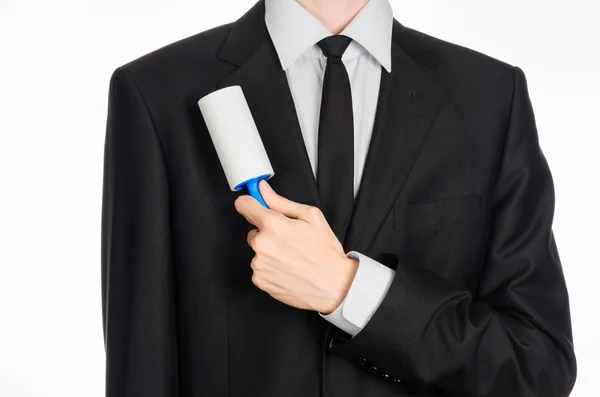 Chemische Reinigung und Business-Thema: Ein Mann im schwarzen Anzug hält eine blaue klebrige Bürste in der Hand, um Kleidung und Möbel von Staub auf weißem Hintergrund im Studio zu reinigen. — Stockfoto