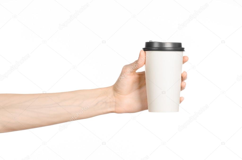 Breakfast and coffee theme: man's hand holding white empty paper coffee cup with a brown plastic cap isolated on a white background in the studio, advertising coffee