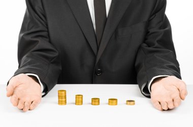 Money and business theme: a man in a black suit indicates the chart bars of gold coins on a white table in the studio on a white background isolated