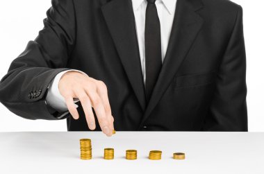 Money and business theme: a man in a black suit indicates the chart bars of gold coins on a white table in the studio on a white background isolated
