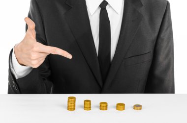 Money and business theme: a man in a black suit indicates the chart bars of gold coins on a white table in the studio on a white background isolated