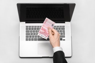 Business and freelance topic: hand in a black suit holding a banknote of 10 euro on a laptop on a white table in the studio isolated top view