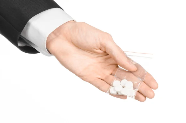 Зависимость и деловая тема: рука в черном костюме держит сумку с белыми таблетками наркотик на белом изолированном фоне в студии — стоковое фото