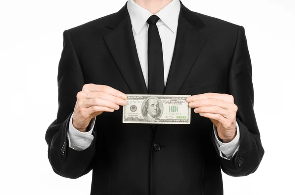 Geld und Geschäftsthema: ein Mann im schwarzen Anzug mit einem Schein über 100 Dollar und einer Handbewegung auf einem isolierten weißen Hintergrund — Stockbild Geld und Geschäftsthema: Ein Mann im schwarzen Anzug hält einen Schein über 100 Dollar in der Hand und zeigt eine Handgeste auf einem isolierten weißen Hintergrund im Studio — Stockfoto