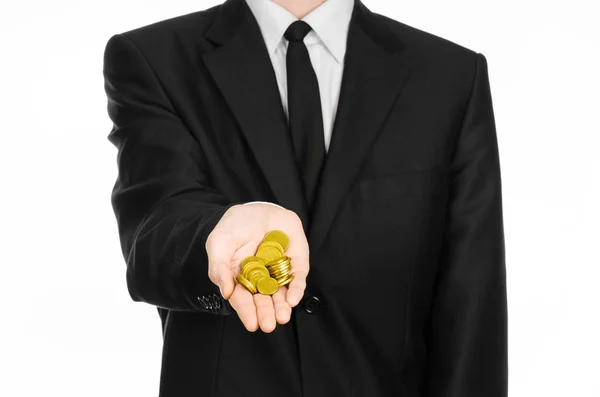 Tema denaro e affari: un uomo in abito nero con in mano un mucchio di monete d'oro in studio su uno sfondo bianco isolato — Foto Stock