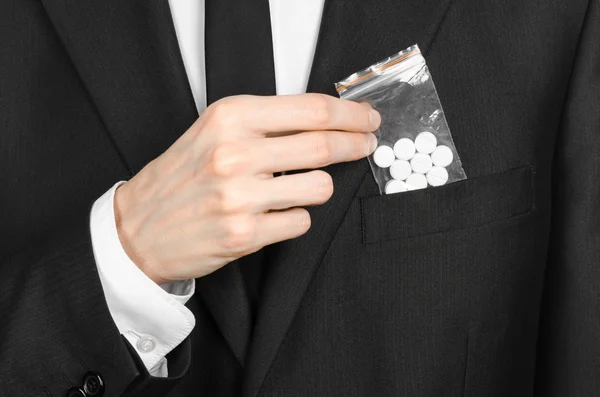Addiction and business topic: hand in a black suit holds bag with white pills a drug on a white isolated background in studio — Stock Photo, Image