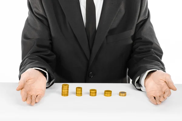 Money and business theme: a man in a black suit indicates the chart bars of gold coins on a white table in the studio on a white background isolated — Stockfoto