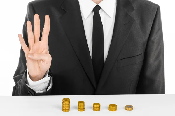 Dinheiro e tema de negócios: um homem em um terno preto indica as barras de cartas de moedas de ouro em uma mesa branca no estúdio em um fundo branco isolado — Fotografia de Stock