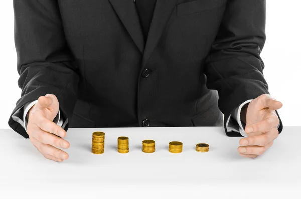 Dinheiro e tema de negócios: um homem em um terno preto indica as barras de cartas de moedas de ouro em uma mesa branca no estúdio em um fundo branco isolado — Fotografia de Stock