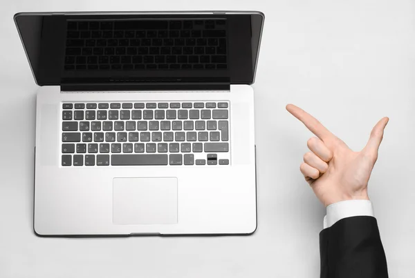 Tema de negocios y tecnología: la mano del hombre en un traje negro mostrando gesto contra un portátil de fondo gris y blanco en el estudio vista superior aislada — Foto de Stock