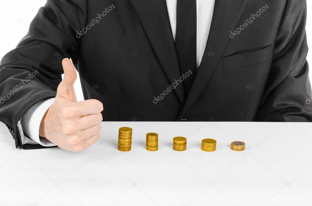 Money and business theme: a man in a black suit indicates the chart bars of gold coins on a white table in the studio on a white background isolated