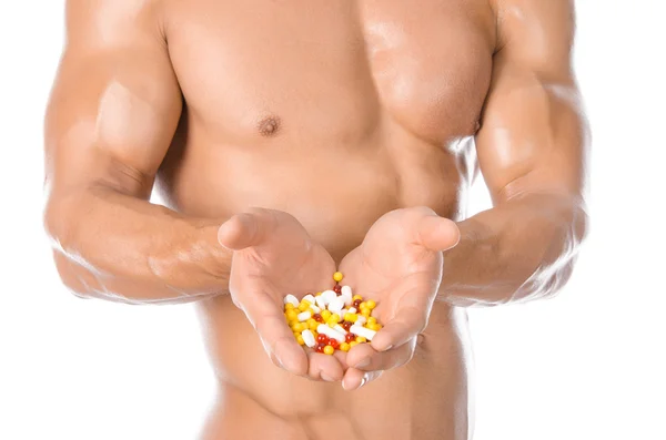 Musculação e aditivos químicos: fisiculturista forte bonito segurando pílulas coloridas isoladas em fundo branco no estúdio — Fotografia de Stock