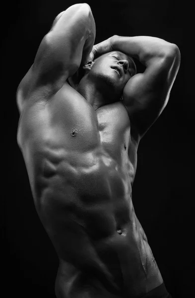 Bodybuilder and strip theme: beautiful with pumped muscles naked man posing in the studio on a dark background, black-and-white photo — Stock Photo, Image