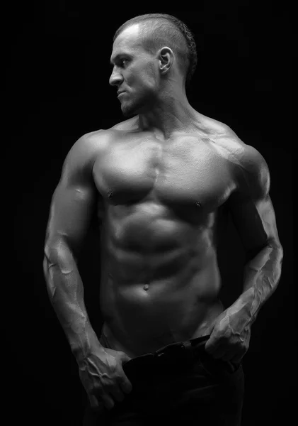 Culturista y tema de la tira: hermosa con músculos bombeados hombre desnudo posando en el estudio sobre un fondo oscuro, foto en blanco y negro —  Fotos de Stock