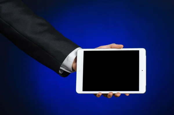 Presentation and business theme: a man in a black suit holding a white tablet touch computer gadget with touch blank black screen on a dark blue background in studio isolated — 스톡 사진