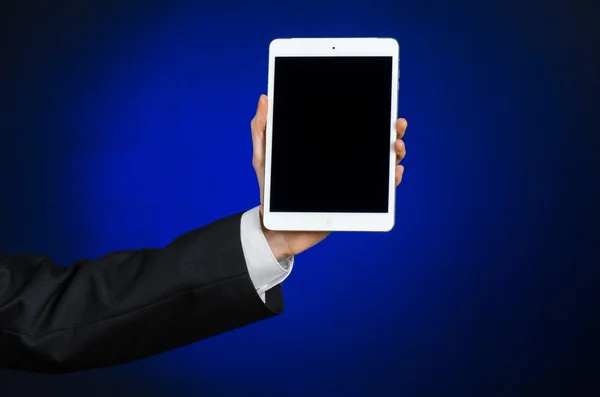 Presentation and business theme: a man in a black suit holding a white tablet touch computer gadget with touch blank black screen on a dark blue background in studio isolated — ストック写真