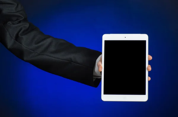 Presentation and business theme: a man in a black suit holding a white tablet touch computer gadget with touch blank black screen on a dark blue background in studio isolated — Φωτογραφία Αρχείου