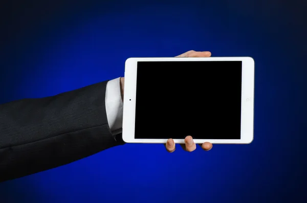 Presentation and business theme: a man in a black suit holding a white tablet touch computer gadget with touch blank black screen on a dark blue background in studio isolated — 스톡 사진