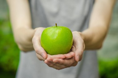 Vejetaryenler ve taze meyve ve sebze Tema niteliğine: bir yeşil elma yeşil çim bir arka plan üzerinde tutan eller