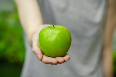 Vejetaryenler ve taze meyve ve sebze Tema niteliğine: bir yeşil elma yeşil çim bir arka plan üzerinde tutan eller