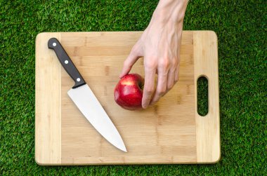 Vejetaryenler ve Tema doğa üzerinde pişirme: bir bıçak ve Kırmızı elma bir kesme tahtası ve yeşil çim üstten görünüm arka plan üzerinde tutan eller