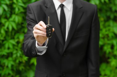 Yeni araba ve iş Tema: siyah elbiseli bir adam yeni bir araba anahtarları yeşil çim bir arka plan üzerinde tutar.