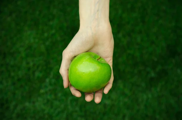 Vegetarianos e frutas e legumes frescos sobre a natureza do tema: mão humana segurando uma maçã verde em um fundo de grama verde vista superior — Fotografia de Stock