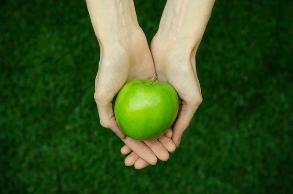 Vegetarianos e frutas e legumes frescos sobre a natureza do tema: mão humana segurando uma maçã verde em um fundo de grama verde vista superior — Fotografia de Stock