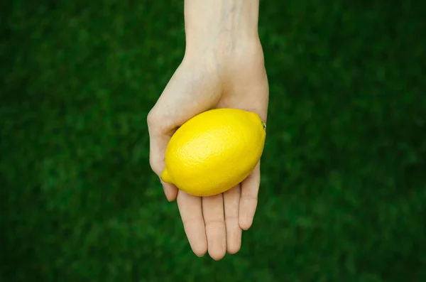 Vegetarians and fresh fruit and vegetables on the nature of the theme: human hand holding a lemon on a background of green grass top view — Stock Photo, Image