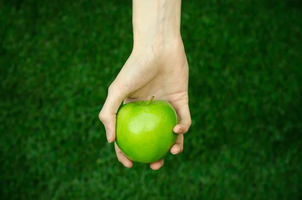 Vegetarianos e frutas e legumes frescos sobre a natureza do tema: mão humana segurando uma maçã verde em um fundo de grama verde vista superior — Fotografia de Stock