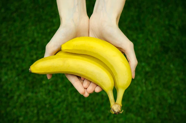 Vegetarianos y frutas y verduras frescas sobre la naturaleza del tema: mano humana sosteniendo un montón de plátanos sobre un fondo de hierba verde vista superior —  Fotos de Stock