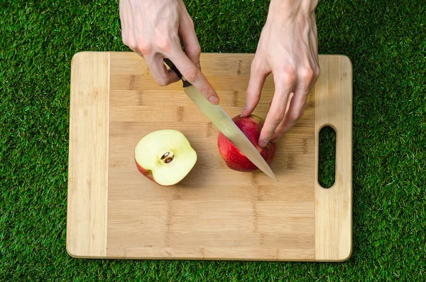 Vegetarianos y cocina sobre la naturaleza del tema: mano humana sosteniendo un cuchillo y una manzana roja en el fondo de una tabla de cortar y césped verde vista superior —  Fotos de Stock