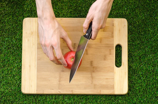 Vegetariani e cucina sulla natura del tema: mano umana che tiene un coltello e tagliere di pomodoro su uno sfondo di erba verde e vista dall'alto — Foto Stock