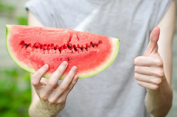 Summer and fresh watermelon theme: a man holds a slice of watermelon on a green background — Stock Photo, Image