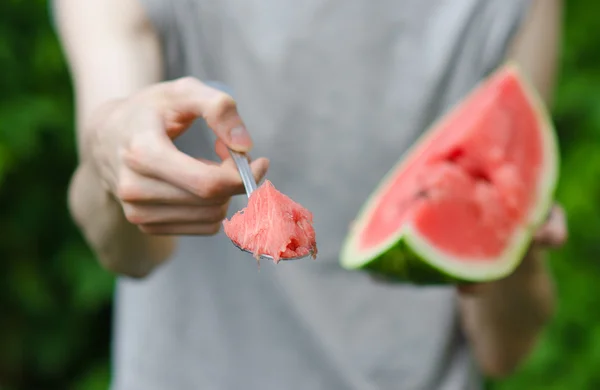 Summer and fresh watermelon theme: a man holds out a spoon with watermelon on the green background — Stock Photo, Image