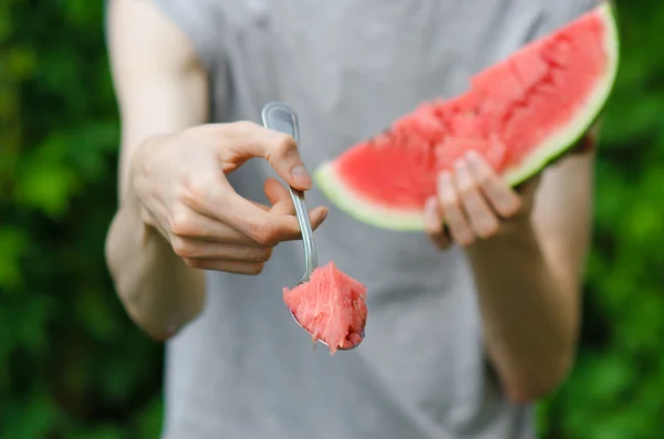 Summer and fresh watermelon theme: a man holds out a spoon with watermelon on the green background — Stock Photo, Image