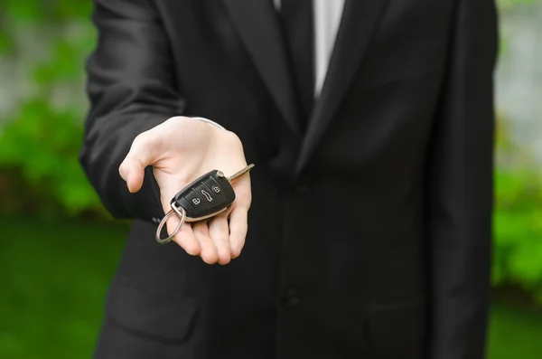 Nieuwe auto en zakelijke thema: een man in een zwart pak omvat de sleutels van een nieuwe auto tegen een achtergrond van groen gras — Stockfoto